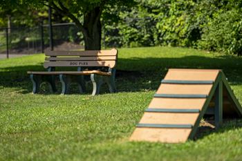 A wooden bench with the words "DOG PARK" on it sits in the grass next to a wooden ramp.